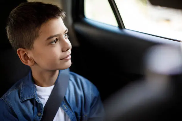 A young boy looking at the window of the car