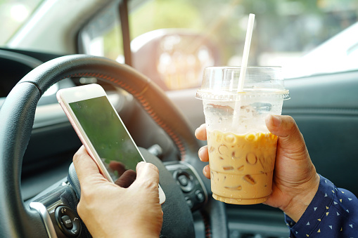 A driver holding a phone and an iced coffee
