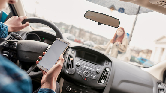 person looking at phone while other hand is on steering wheel