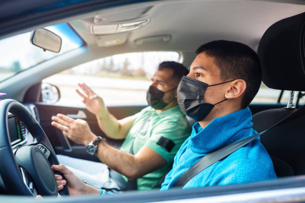 A beginner driver and the instructor talking to each other while wearing masks