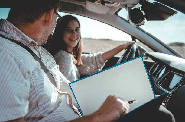 A beginner driver smiling at her instructor who is holding a checklist