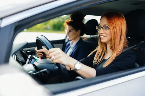 female student driving while driving instructor watches