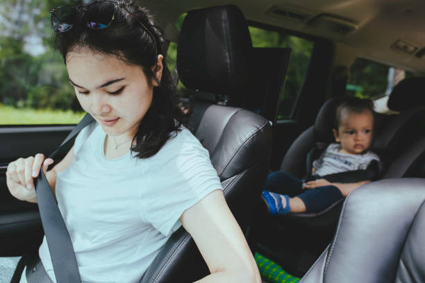 A woman putting on her seatbelt and a baby at the back with a seatbelt on